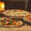 Trio of gourmet pizzas with unique toppings near a wood-fired oven, ideal for food enthusiasts.